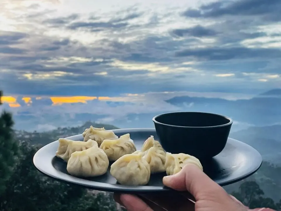 A plate of delicious momos held up against a breathtaking Himalayan sunrise