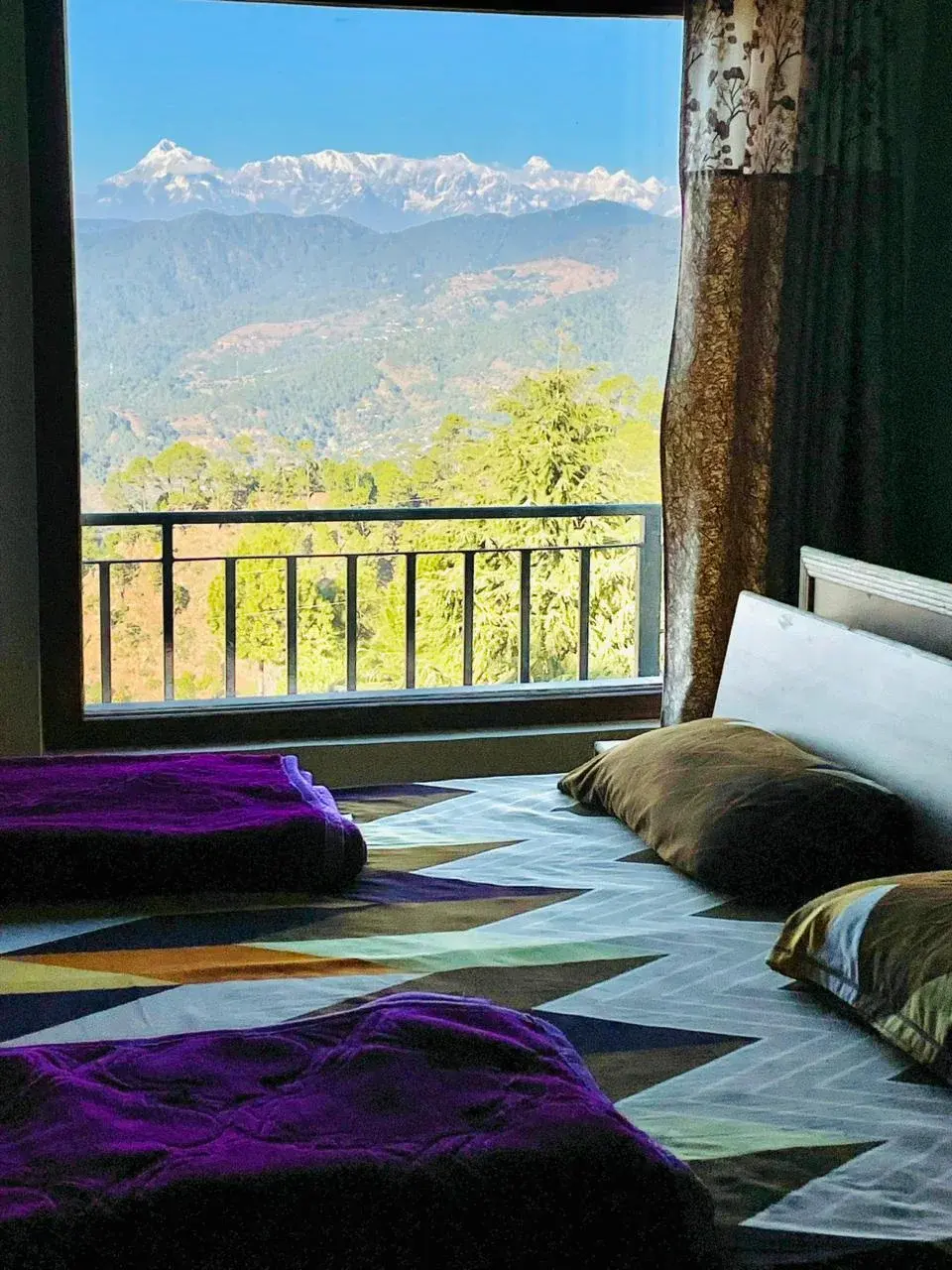 Comfortable bed with purple blankets looking out to a clear view of the Himalayan peaks