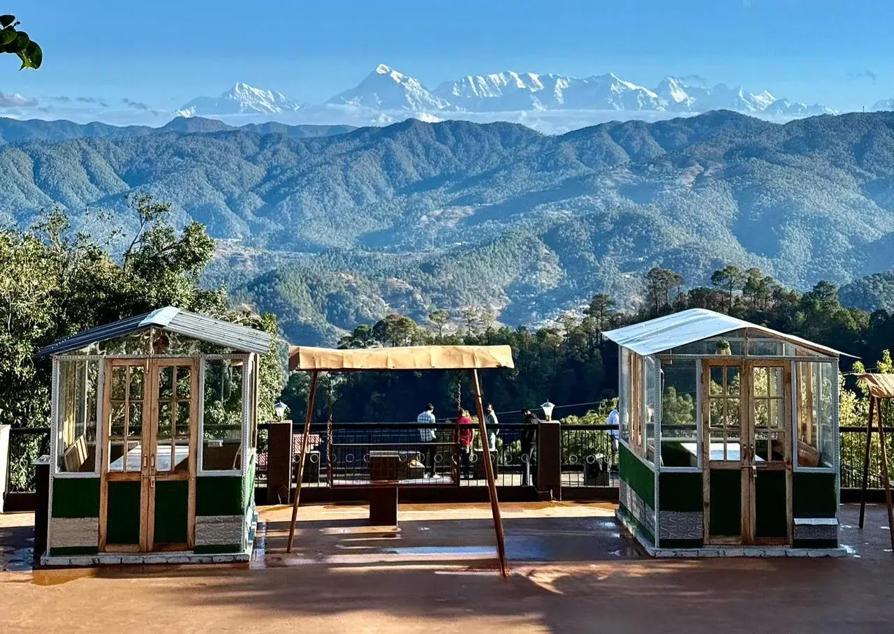 Hotel Royal Monal open terrace with seating areas overlooking rolling green hills and majestic Himalayan mountains
