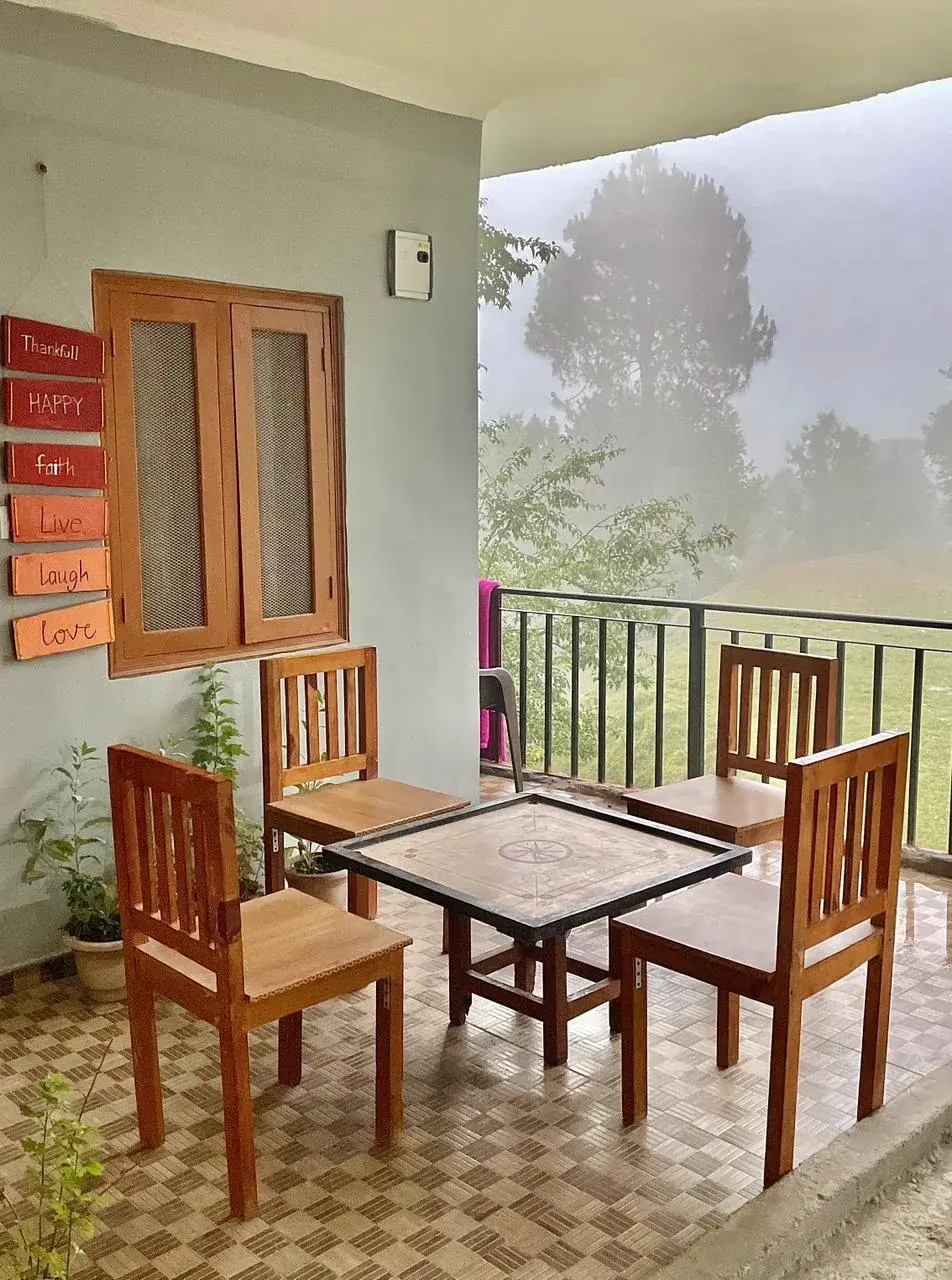 Outdoor balcony seating area featuring wooden chairs and table with misty mountain views